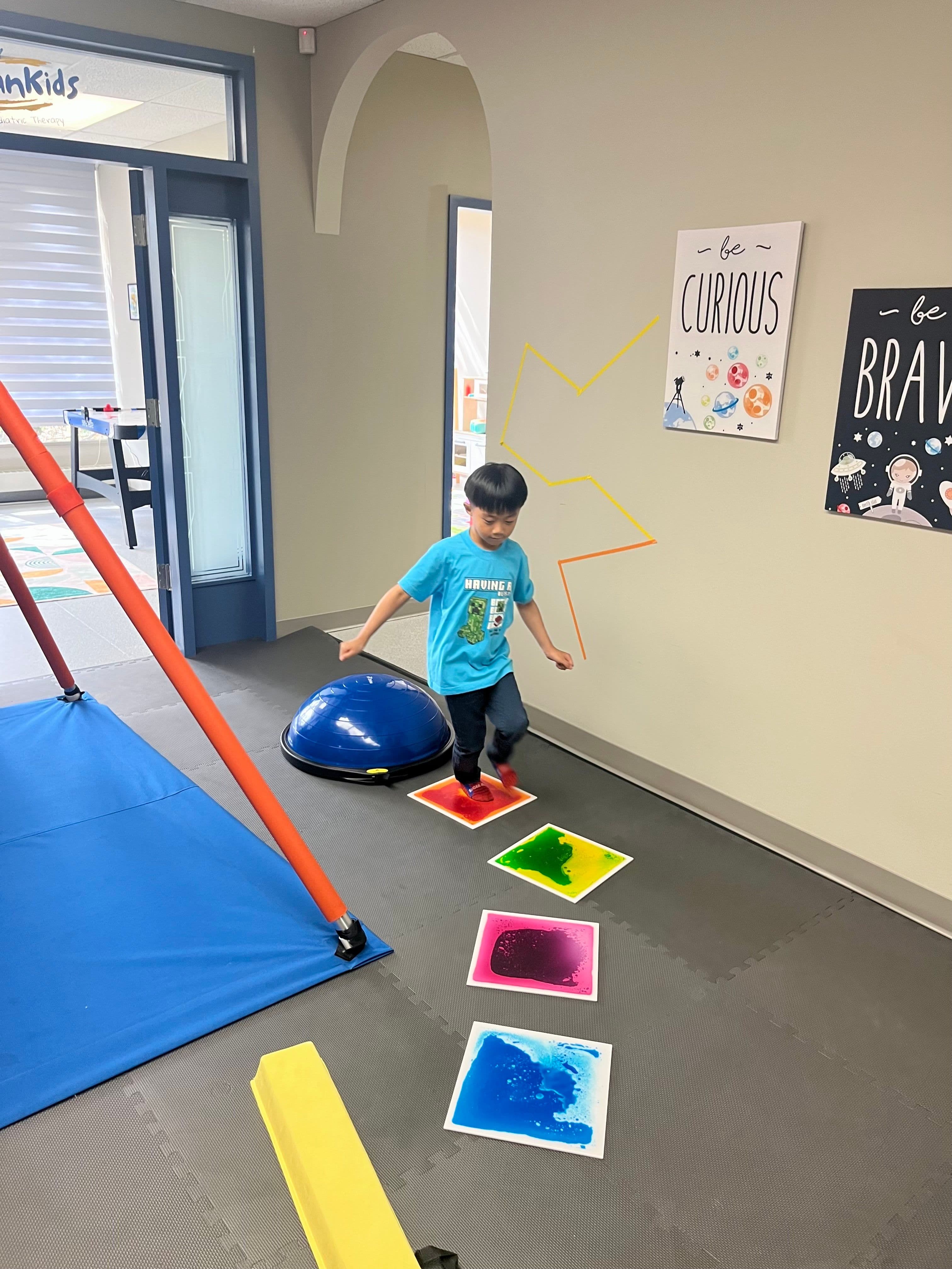 A boy stepping from one liquid sensory tile to the next along a path laid across the floor, with a balance dome behind him.