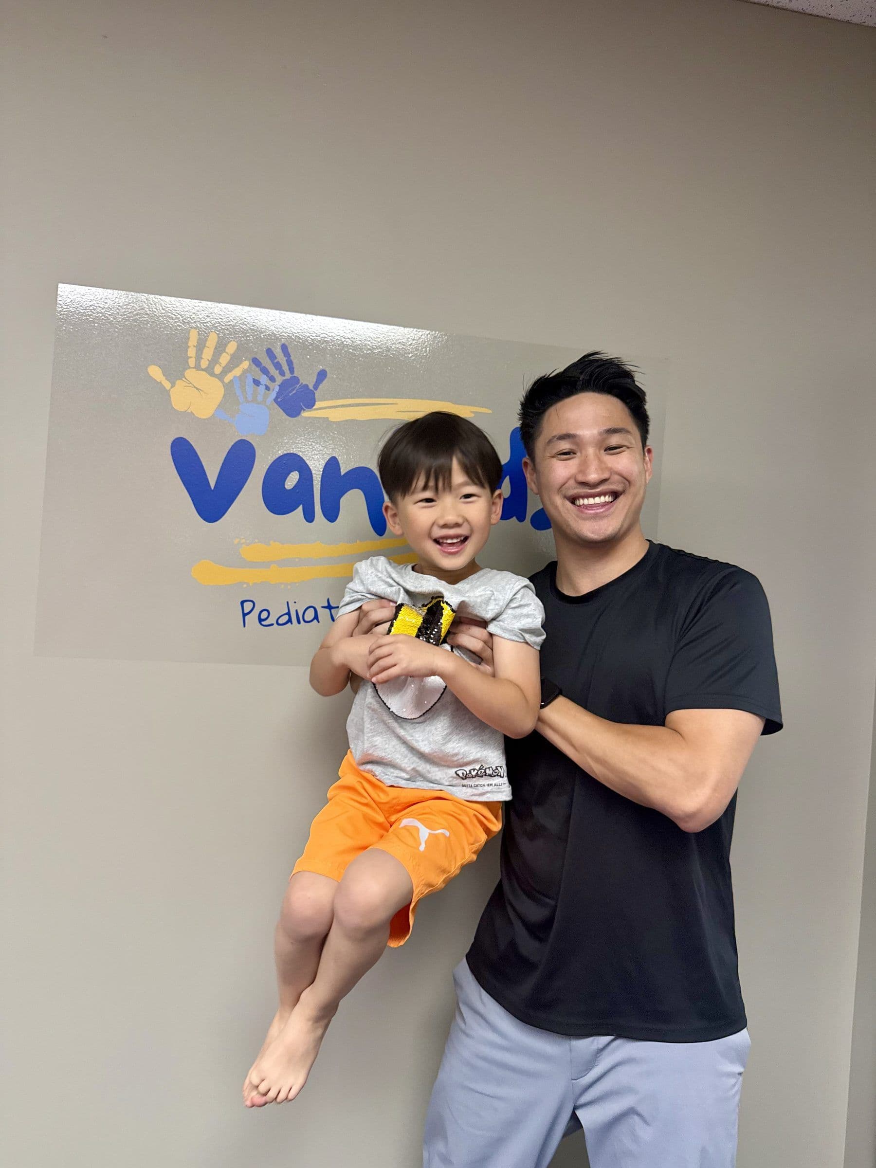 Leonardo Tam 抱着一名幼童,身后是 VanKids 诊所招牌。