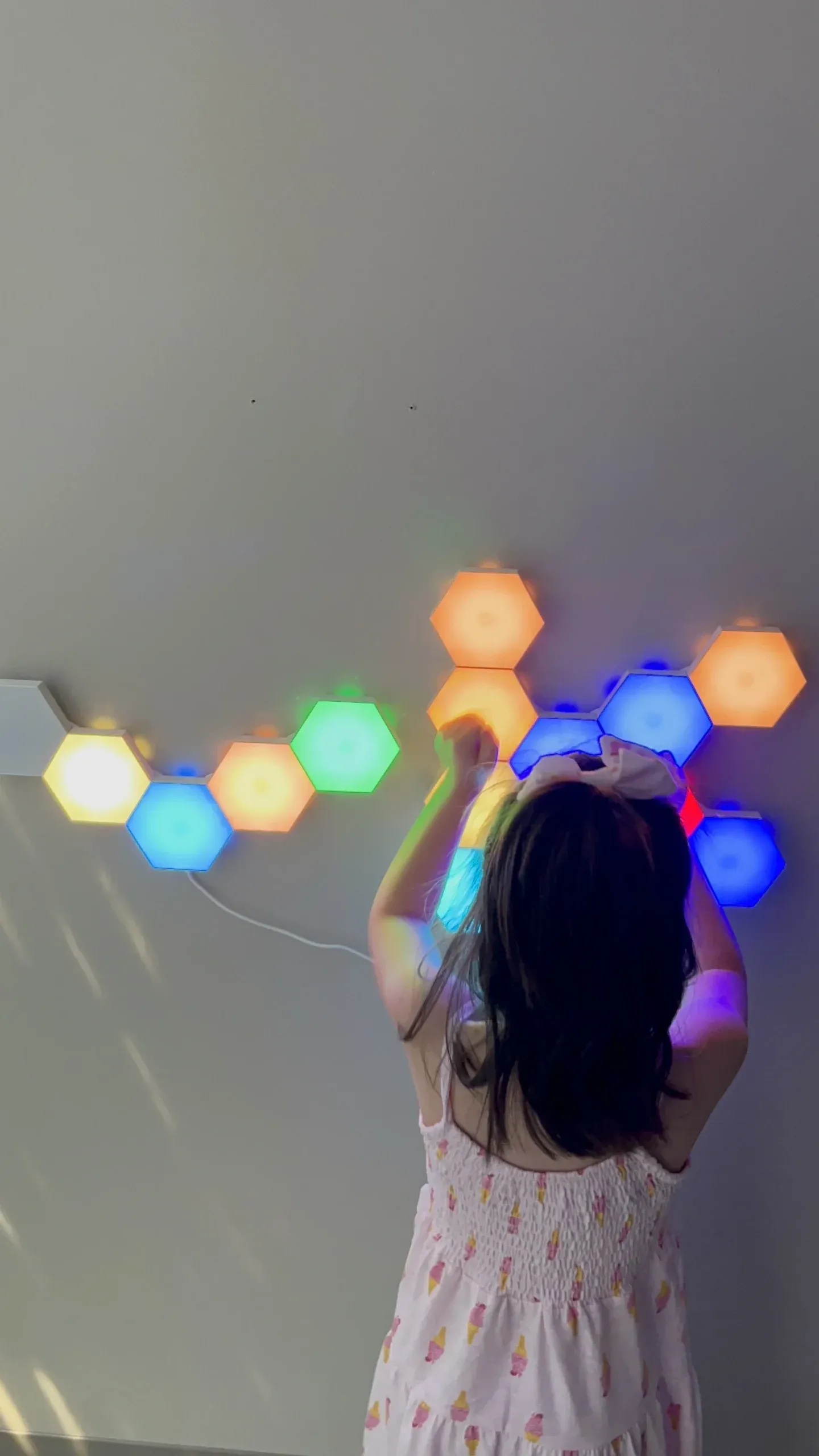 A child reaches toward glowing hexagonal wall lights in a dim sensory room.